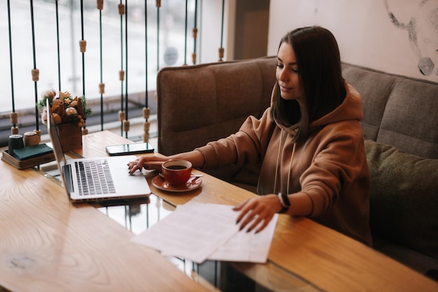 A person is working on a laptop at a home office. They are surrounded by tax documents, a calculator, and a cup of coffee. A window provides natural light.